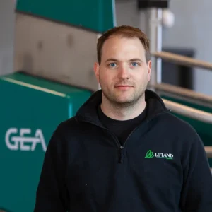 En mann i en svart Lifland-genser står ved siden av grønt utstyr merket med "GEA", som legemliggjør essensen av Liflands innovative tilnærming.