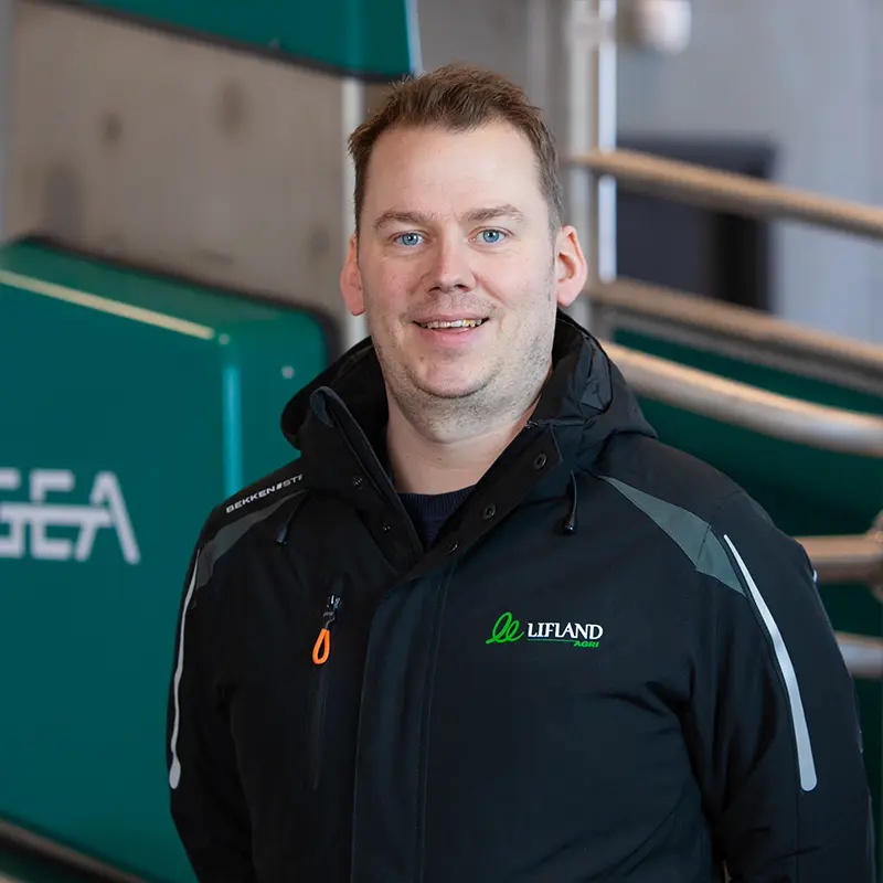 En person som har på seg en svart GEA-jakke står innendørs i nærheten av metallrekkverket, virker dypt i tanker, kanskje vurderer sitt neste lifland-eventyr eller venter på en viktig kontakt.