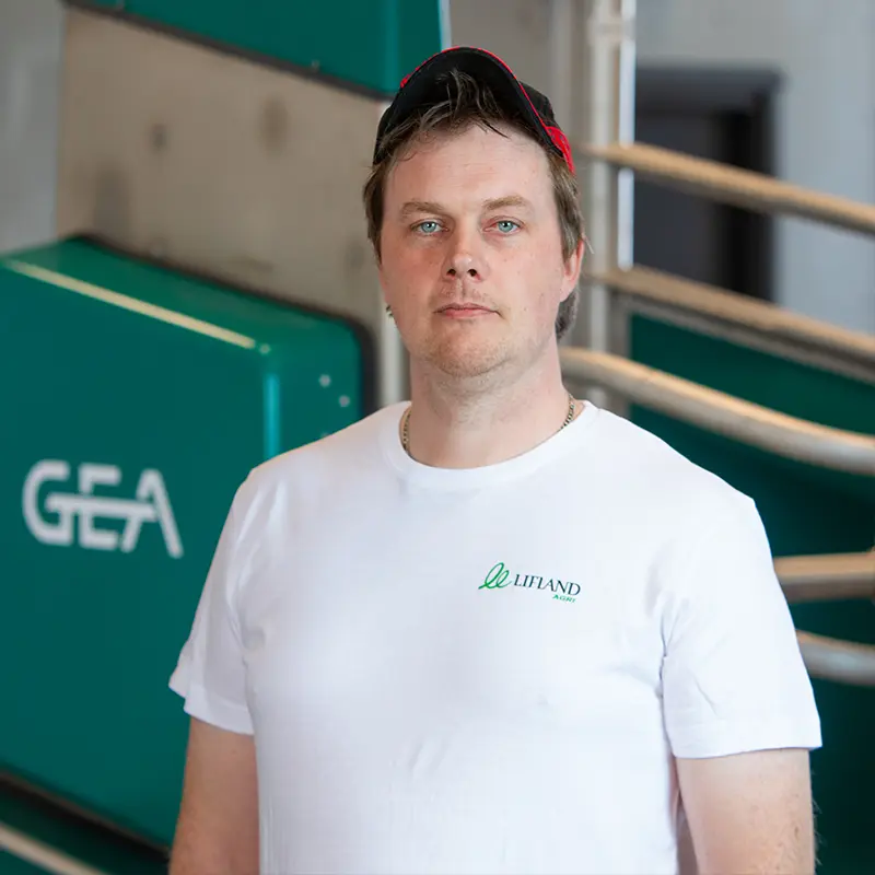 En mann i hvit skjorte og caps står foran metallstenger og observerer nøye en blågrønn maskin merket «GEA», og vurderer tilsynelatende hvordan den kan forbedres for Lifland Kontakts banebrytende prosesser.