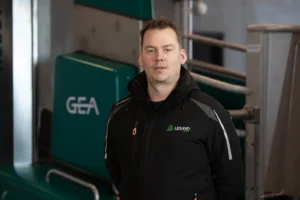 En mann iført svart jakke står innendørs foran grønt og grått industriutstyr merket «GEA». Nysgjerrig på melkerobot? Kent er i Salten-området 23.–27. juni.
