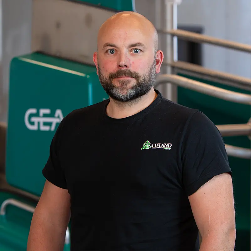 En mann med skjegg og svart t-skjorte står innendørs foran gen GEA melkerobot.