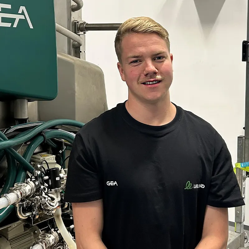 En person med kort, blondt hår står ved siden av en GEA-melkerobot.