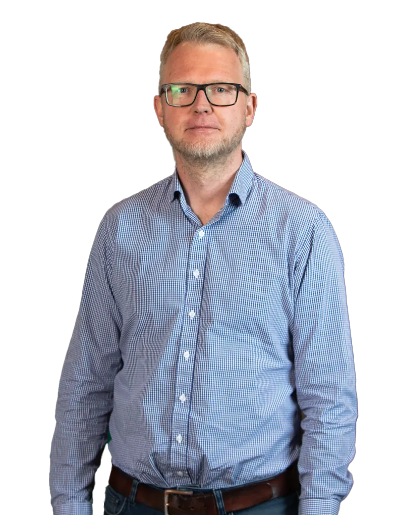 En mann med briller og blårutig skjorte står vendt mot kameraet med et nøytralt uttrykk som minner om en rolig melkerobot.