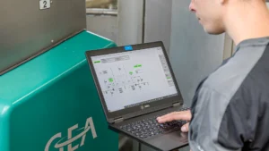 En person bruker en bærbar PC med programvaren Monitor 360 til å overvåke et industrisystem, ved siden av en grønn maskin merket "GEA".